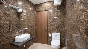 Un baño con pared de mármol, puerta de madera, lavabo blanco y retrete.
