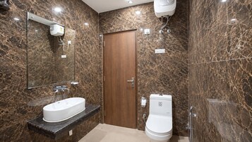 Un baño con pared de mármol, puerta de madera, lavabo blanco y retrete.