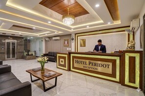 Een hotel receptie met een receptiebalie, een kroonluchter, een beeld en een zithoek met een bijzettafeltje en bloemen.
