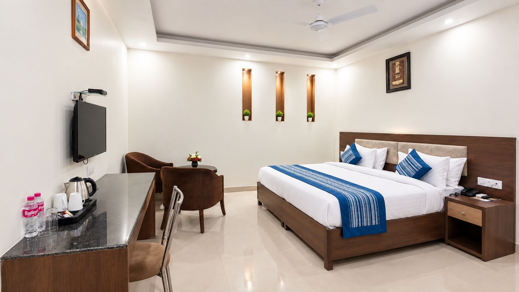 A hotel room with a bed, bedside table, desk, chair, and a television.