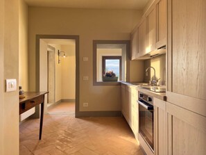 A modern kitchen with wooden cabinets, a built-in oven, and a window with a view. - Casale Tre Dame - Appartamento L Aretino (Castiglion Fiorentino)