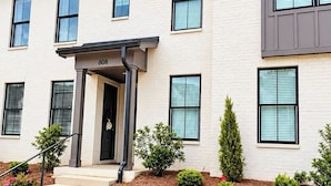 A two-story building with a flat roof, a front entrance with a door, and a number '608' above the door. There are steps leading to the entrance, and the building is surrounded by a landscaped area with various shrubs and plants. - The Archie, 2mi to Campus & Sq Velvet Ditch Villas (Oxford)