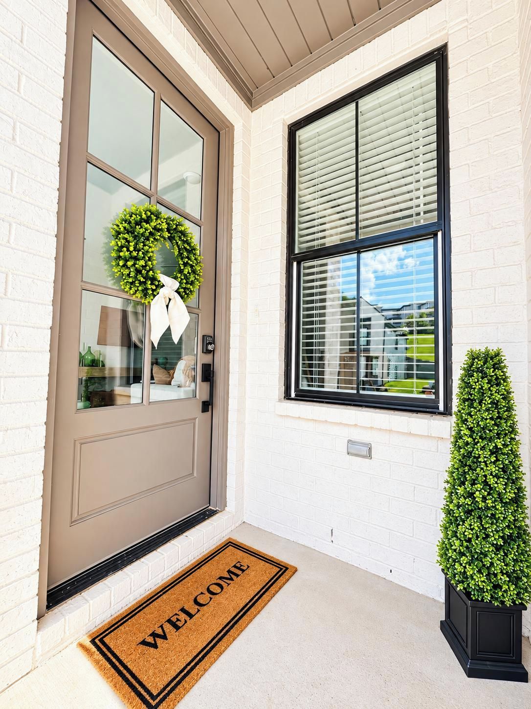 A front door with a welcome mat, a wreath, and a window with blinds.