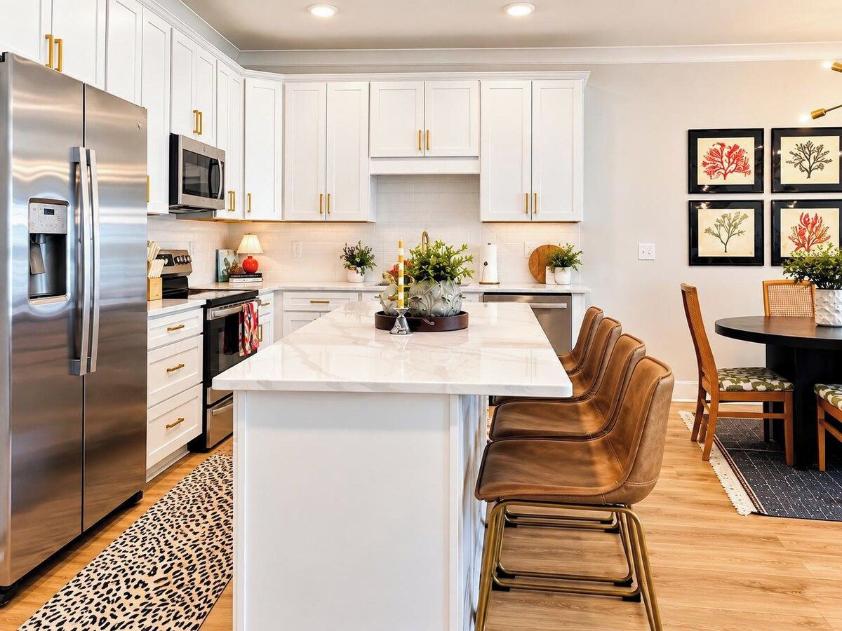 A modern kitchen with white cabinetry, stainless steel appliances, and a central island with bar stools.