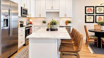 A modern kitchen with white cabinetry, stainless steel appliances, and a central island with bar stools.