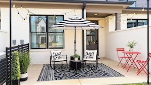 An outdoor patio area with a table and chairs, a striped umbrella, string lights, and a small potted plant. - The Archie, 2mi to Campus & Sq Velvet Ditch Villas (Oxford)