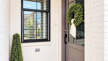 A front door with a 'WELCOME' mat, a potted plant, a wreath, and a window with blinds.