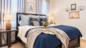 Quarto com cama, mesas de cabeceira, ventilador de teto e decoração náutica.