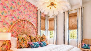 Une chambre à coucher comprenant un lit, une table de chevet, une chaise, une fenêtre avec des rideaux et un ventilateur de plafond.