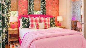 Ein Schlafzimmer mit einem rosa Bett, gemusterten Vorhängen und einem farbenfrohen Teppich.