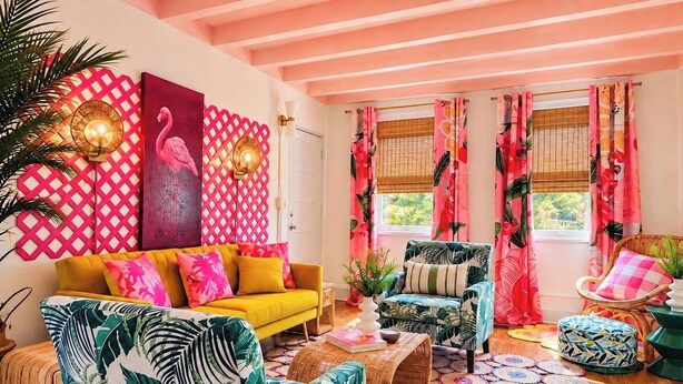 Une pièce avec un canapé jaune, un fauteuil à motifs, une table basse en osier et un tapis aux motifs tropicaux.