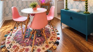 Un coin repas avec une table ronde, des chaises roses, un tapis à motifs et un buffet turquoise agrémenté de lampes.