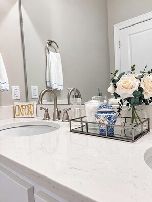A bathroom with a white marble sink, a mirror, a towel rack, and a decorative vase with flowers. - The Lily House, 2mi 2 Sq+Campus, VelvetDitchVillas (Oxford)
