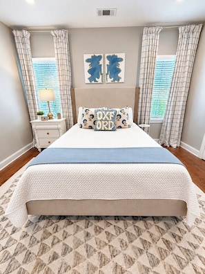 A bedroom with a large bed, two nightstands, a wall-mounted lamp, and a window with curtains.