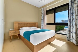 Ein Schlafzimmer mit einem großen Bett, einem Nachttisch, einem Fenster mit Vorhängen und Blick ins Freie.
