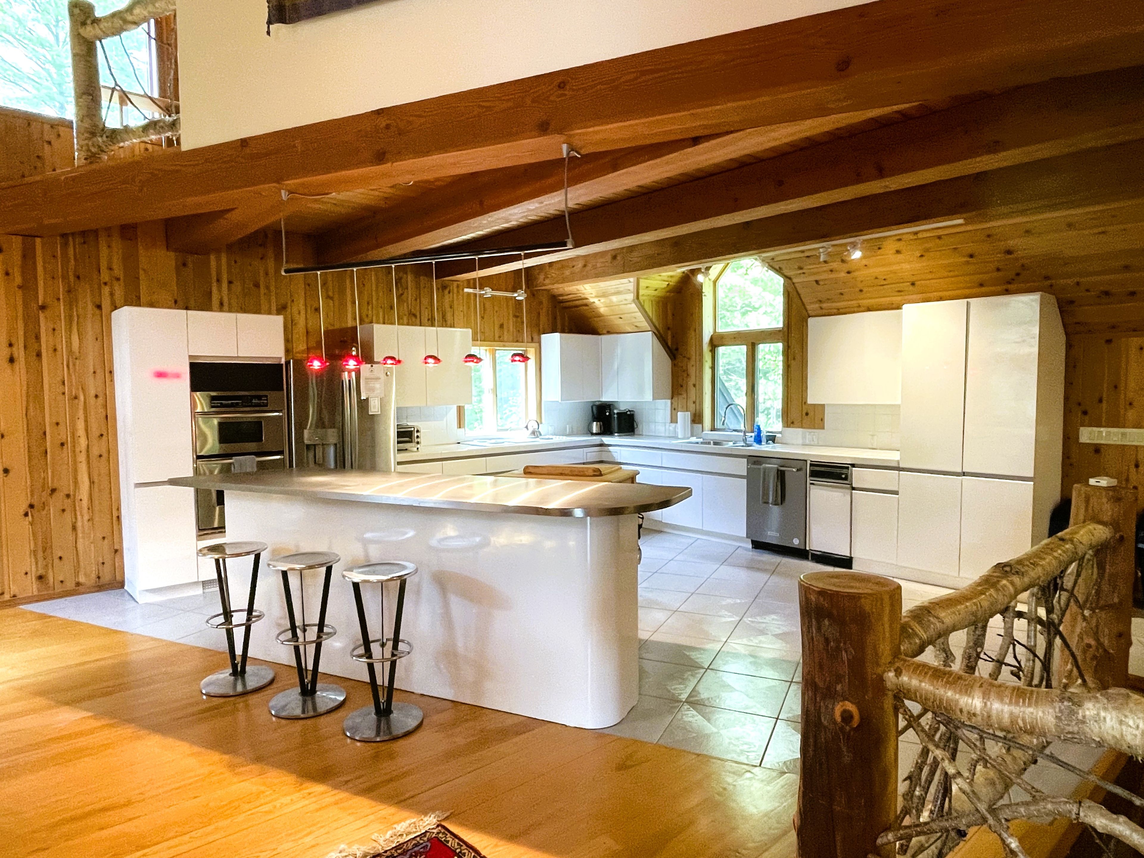 A modern kitchen with wooden beams, white cabinetry, stainless steel appliances, and a central island with bar stools.