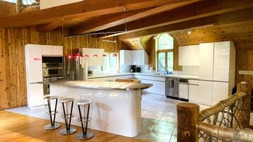 A modern kitchen with wooden beams, white cabinetry, stainless steel appliances, and a central island with bar stools.