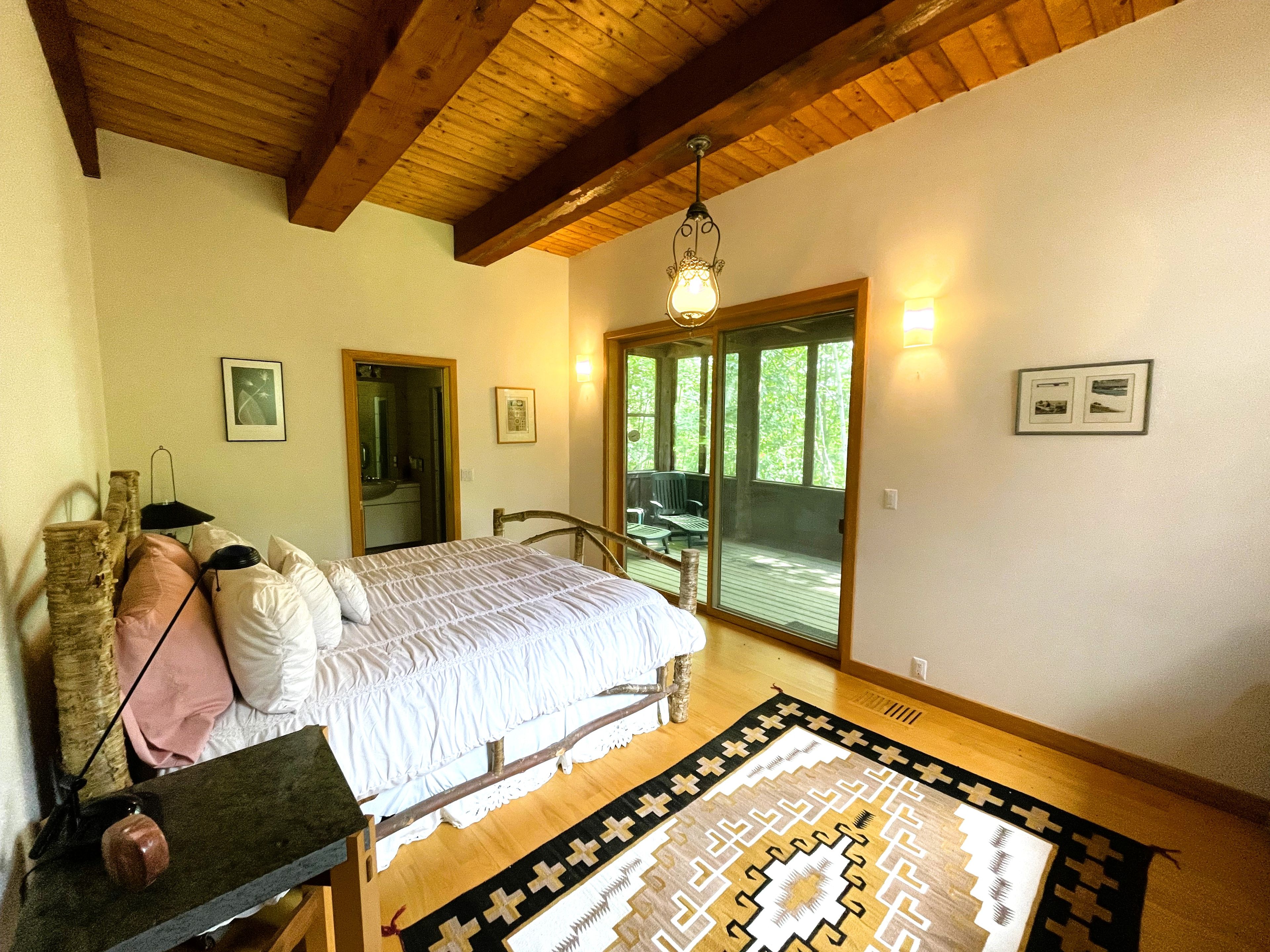 A bedroom with a bed, a nightstand, a mirror, a dresser, a window, and a door leading to a balcony.