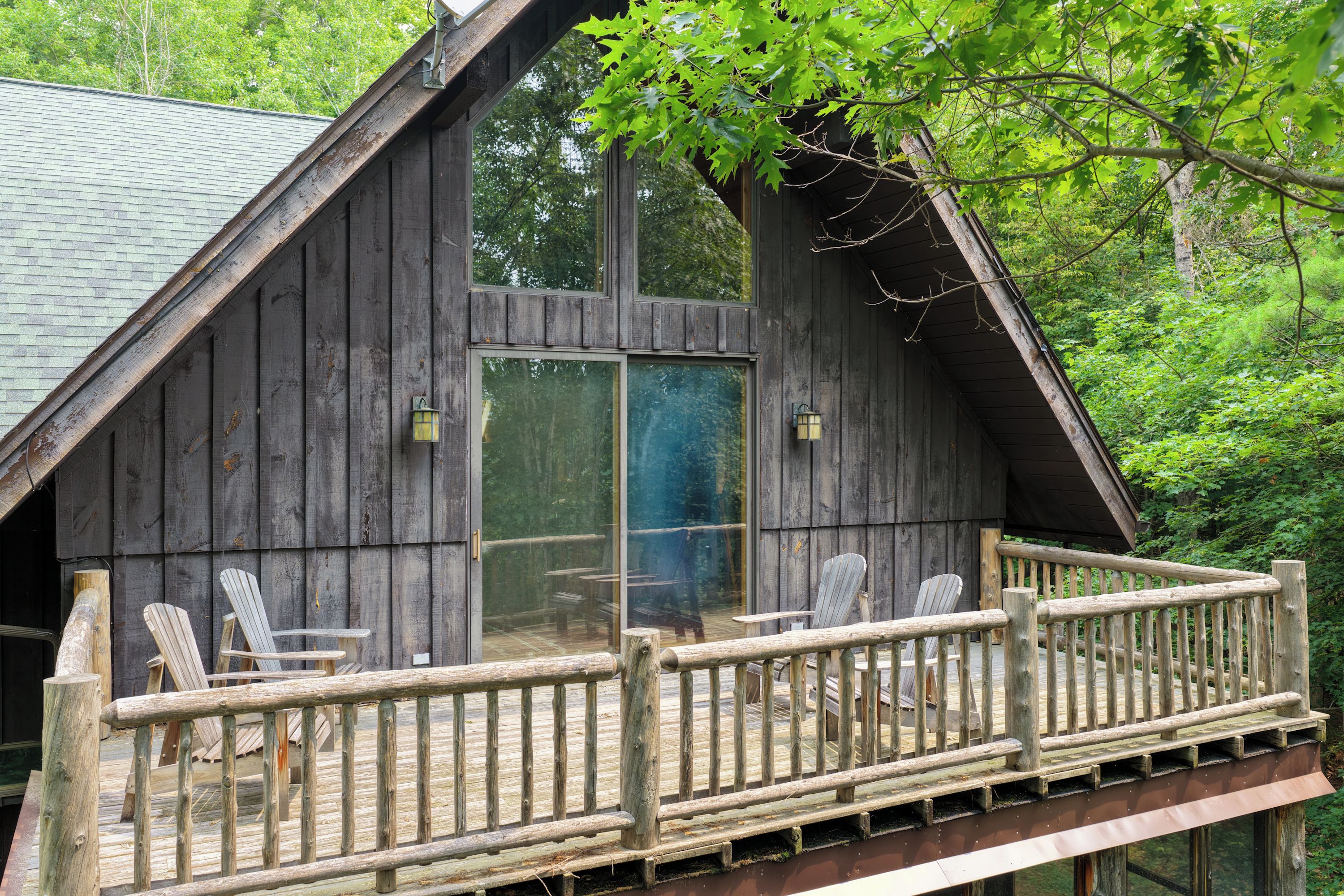 Une cabane en bois dotée d’un balcon, de deux fauteuils Adirondack et d’une porte vitrée.
