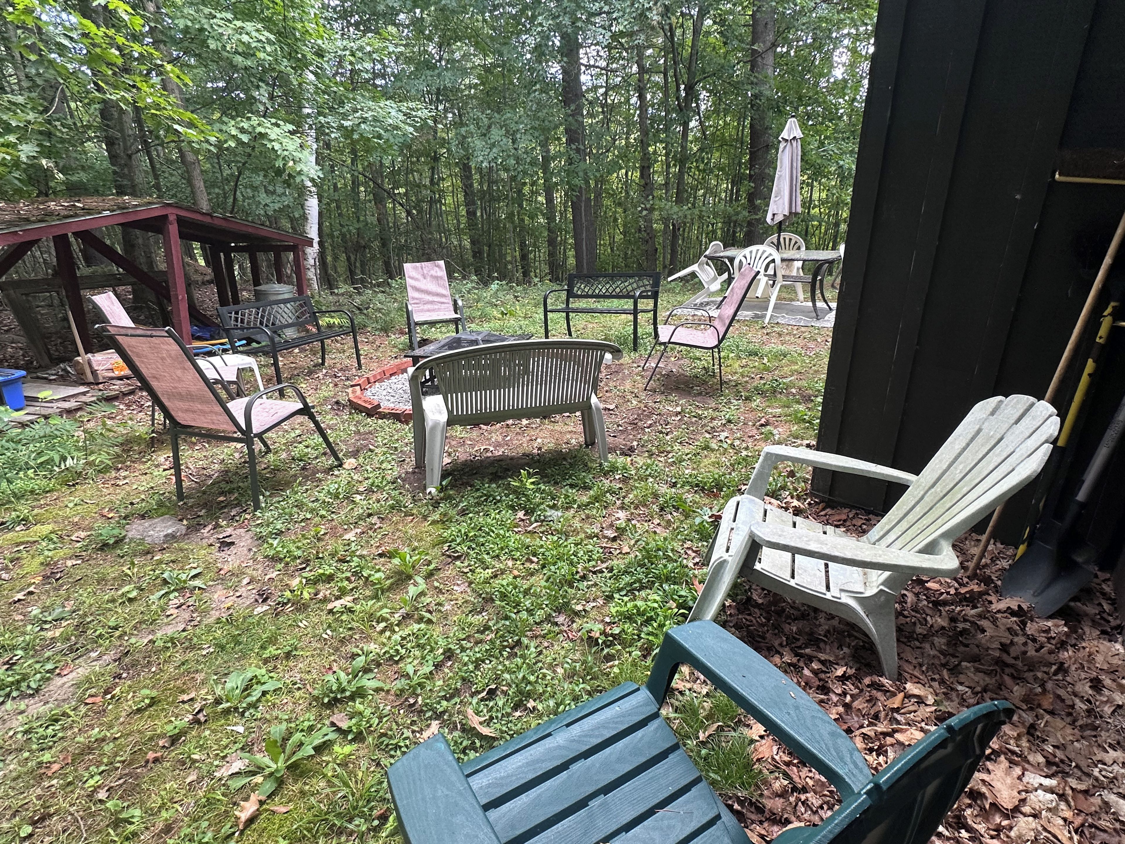 An outdoor seating area with metal chairs and a bench, surrounded by trees.