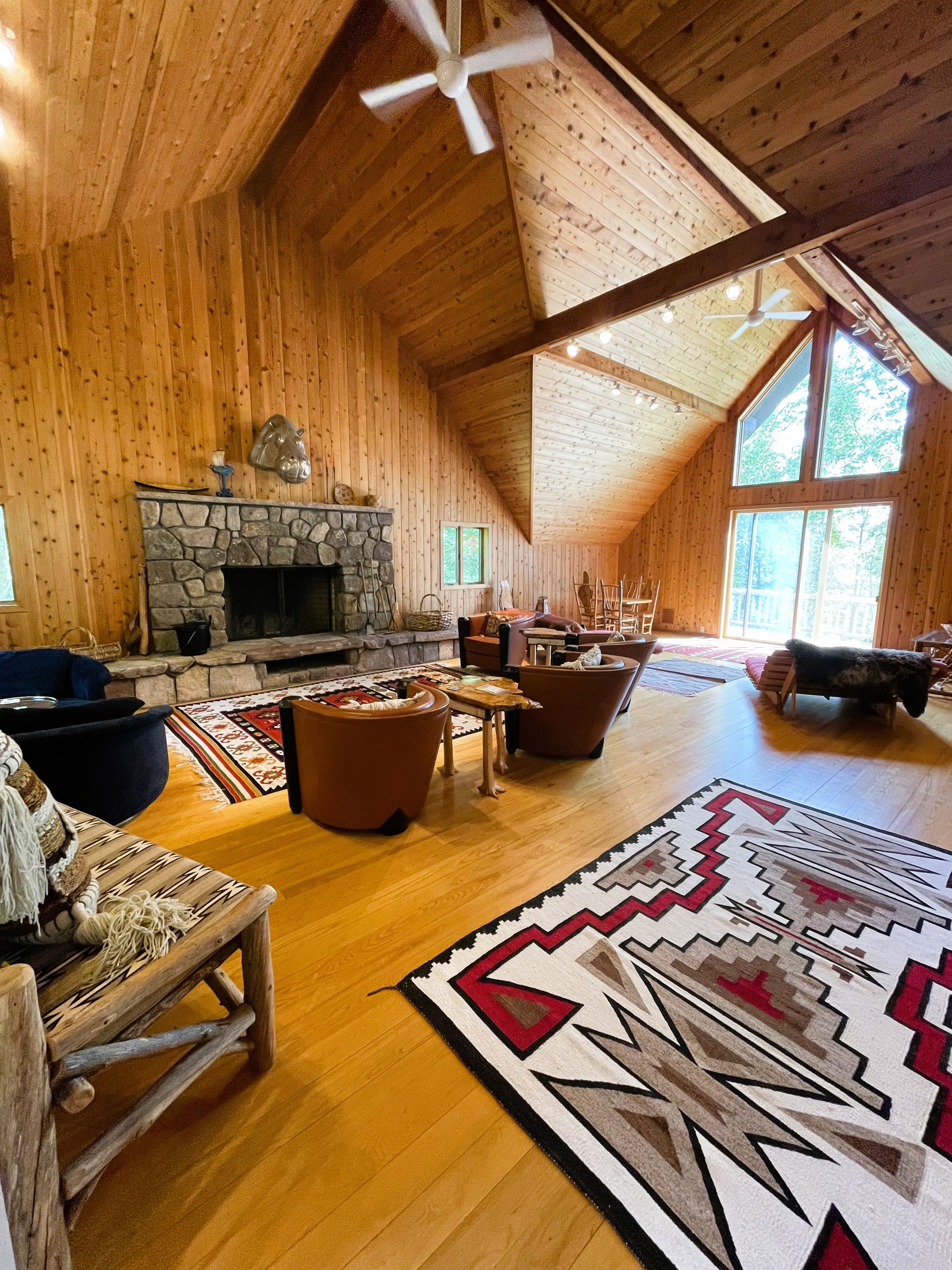 Un intérieur spacieux de chalet en bois, avec une cheminée en pierre, des planchers en bois et une grande fenêtre.