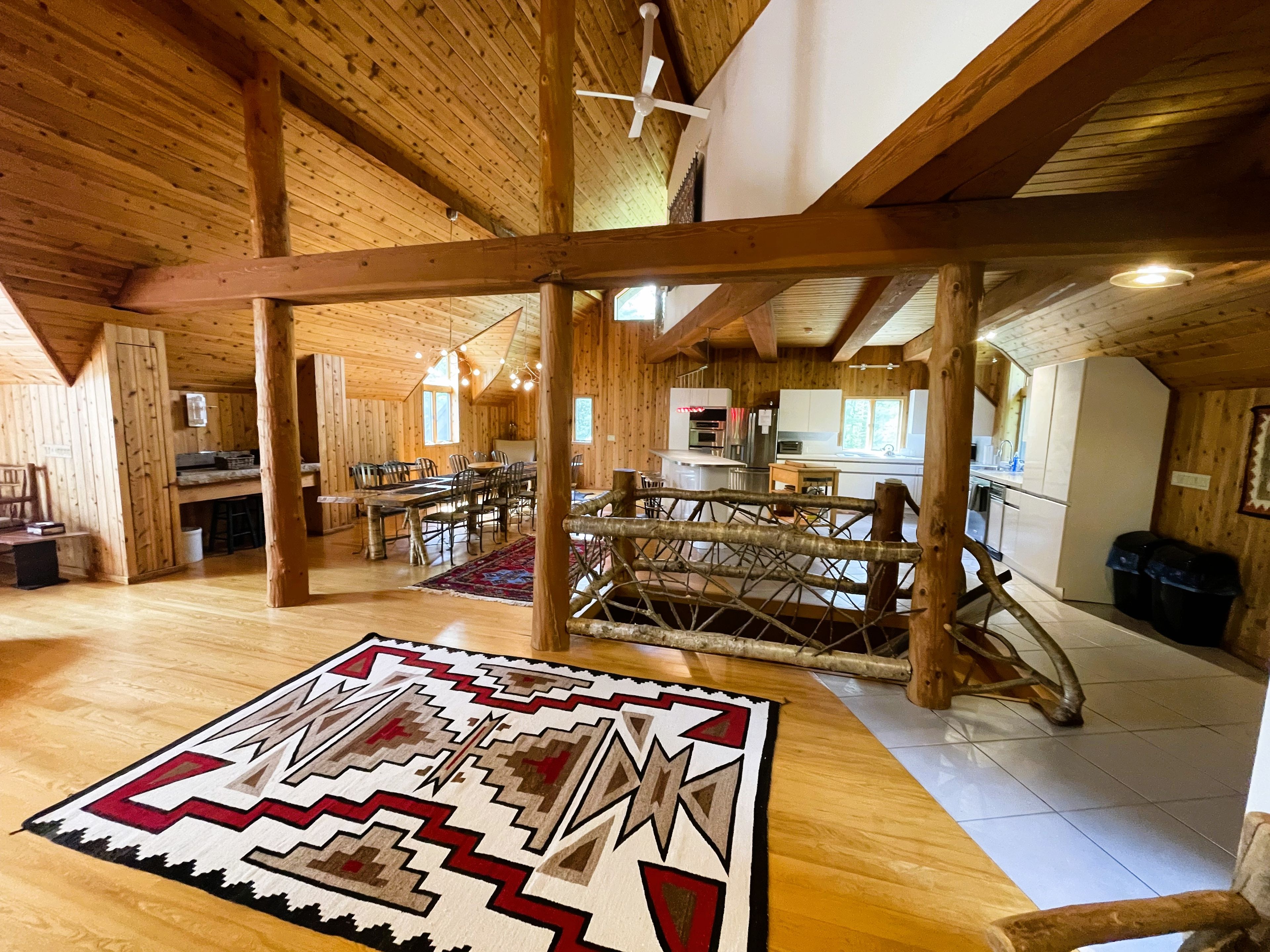 A spacious wooden interior with a dining area, kitchen, and a large rug with a geometric pattern.