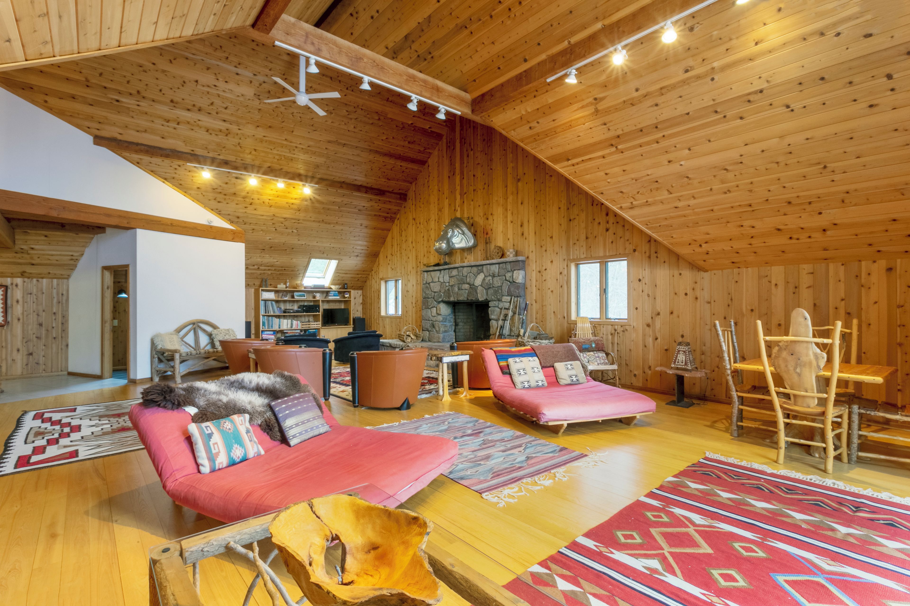 A spacious loft-style living area with a high ceiling, wooden walls, a stone fireplace, and a variety of seating options.