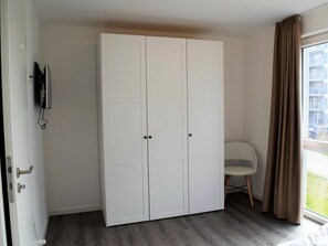A room with a large white wardrobe, a small white chair, and a window with curtains. - House No. 23, Holiday Home Deichgraf (Wangerland)