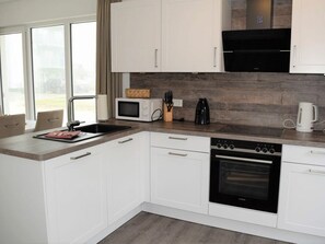 A modern kitchen with white cabinetry, a built-in oven, and a microwave. - House No. 23, Holiday Home Deichgraf (Wangerland)