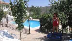 Piscina cercada com espreguiçadeira e uma pessoa próxima.