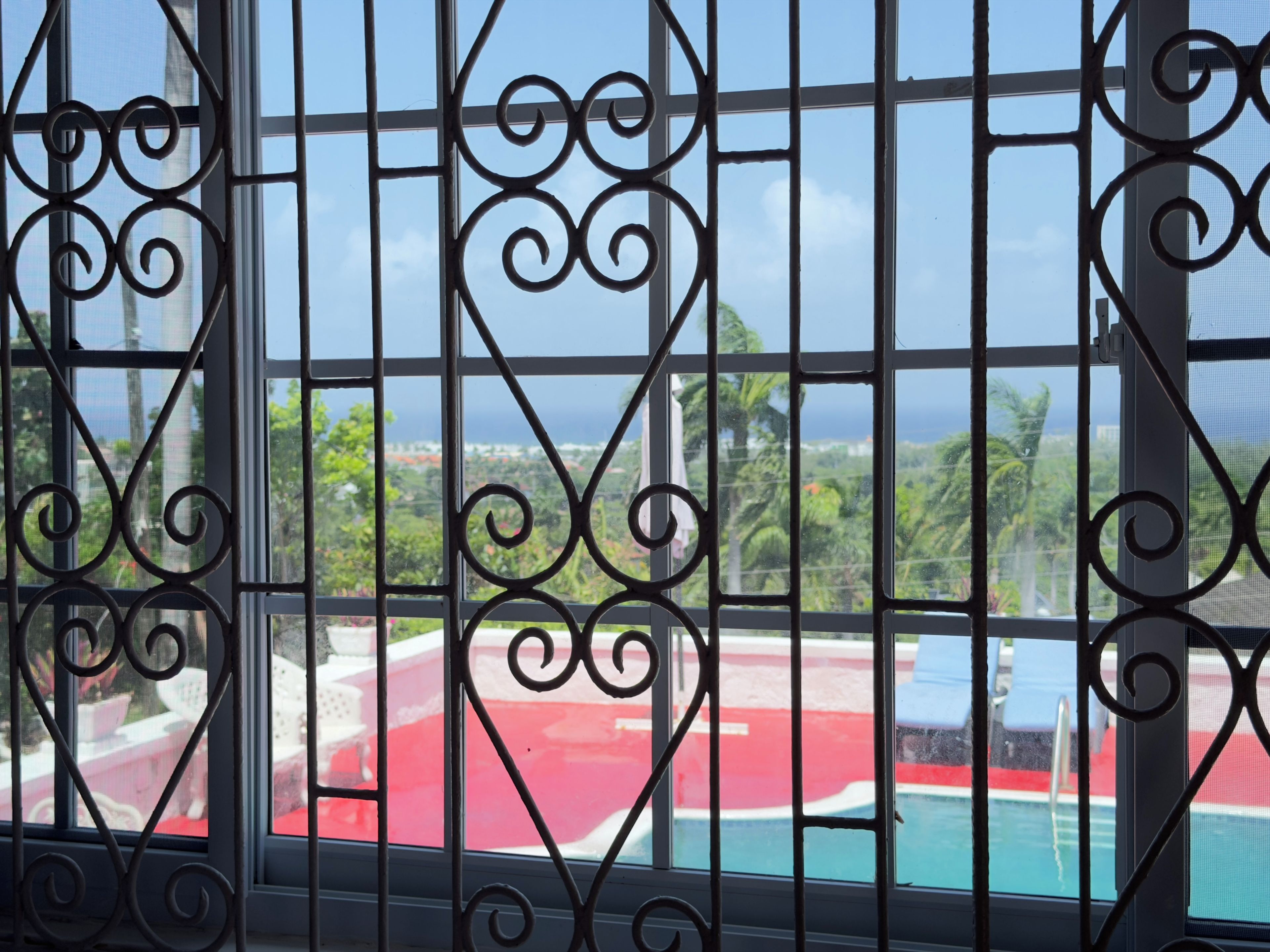 Janela com grades de metal decorativas e vista para a área da piscina.