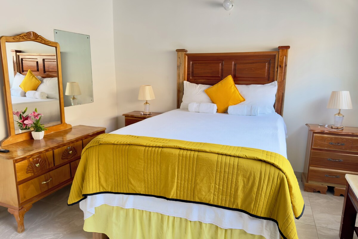 A neatly made bed with a wooden headboard, a bedside table with a lamp, and a mirror on the wall.