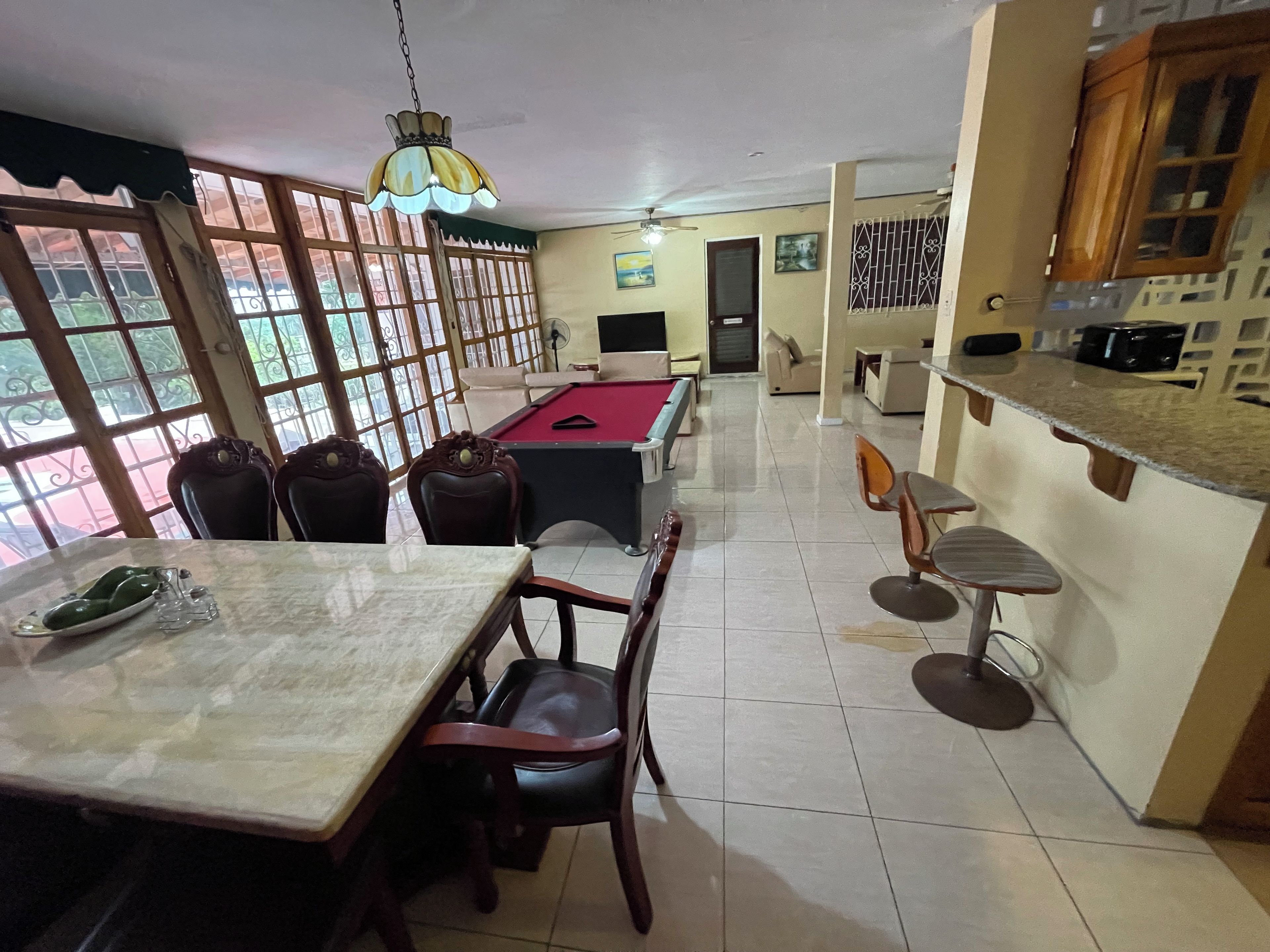 Uma área de refeições com mesa de bilhar, cadeiras e um bar com banquetas.