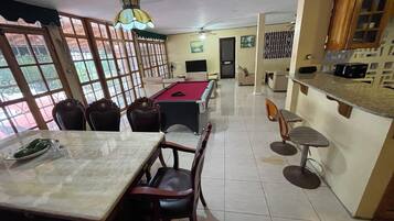 Uma área de refeições com mesa de bilhar, cadeiras e um bar com banquetas.