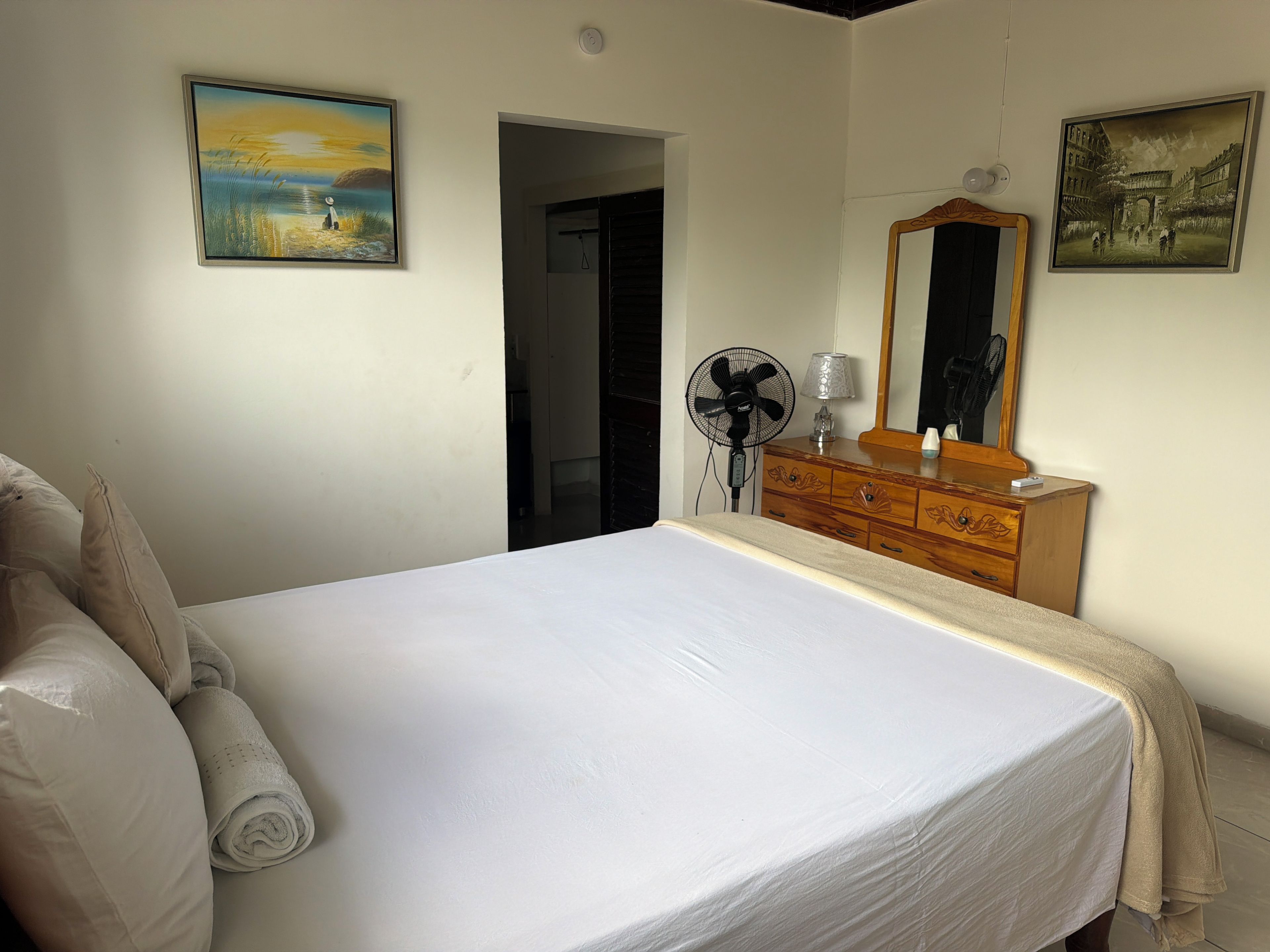 Un dormitorio con una cama, un aparador, un espejo y dos cuadros en la pared.