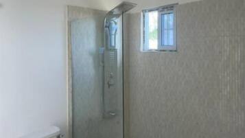 Un baño con inodoro, ducha con mampara de vidrio y una ventana pequeña.