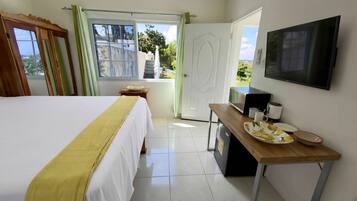 A hotel room with a bed, a desk with a coffee maker, a television, and a window with curtains.