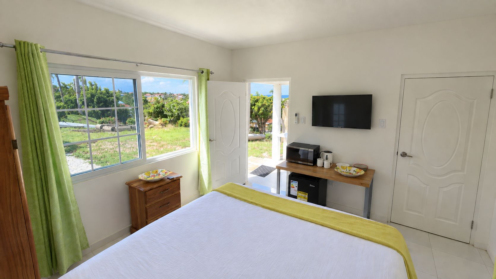 Un dormitorio con cama, escritorio con microondas, televisión y vistas al exterior.
