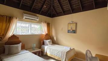 Una habitación con dos camas, ventilador de techo, unidad de aire acondicionado y una ventana con cortinas.