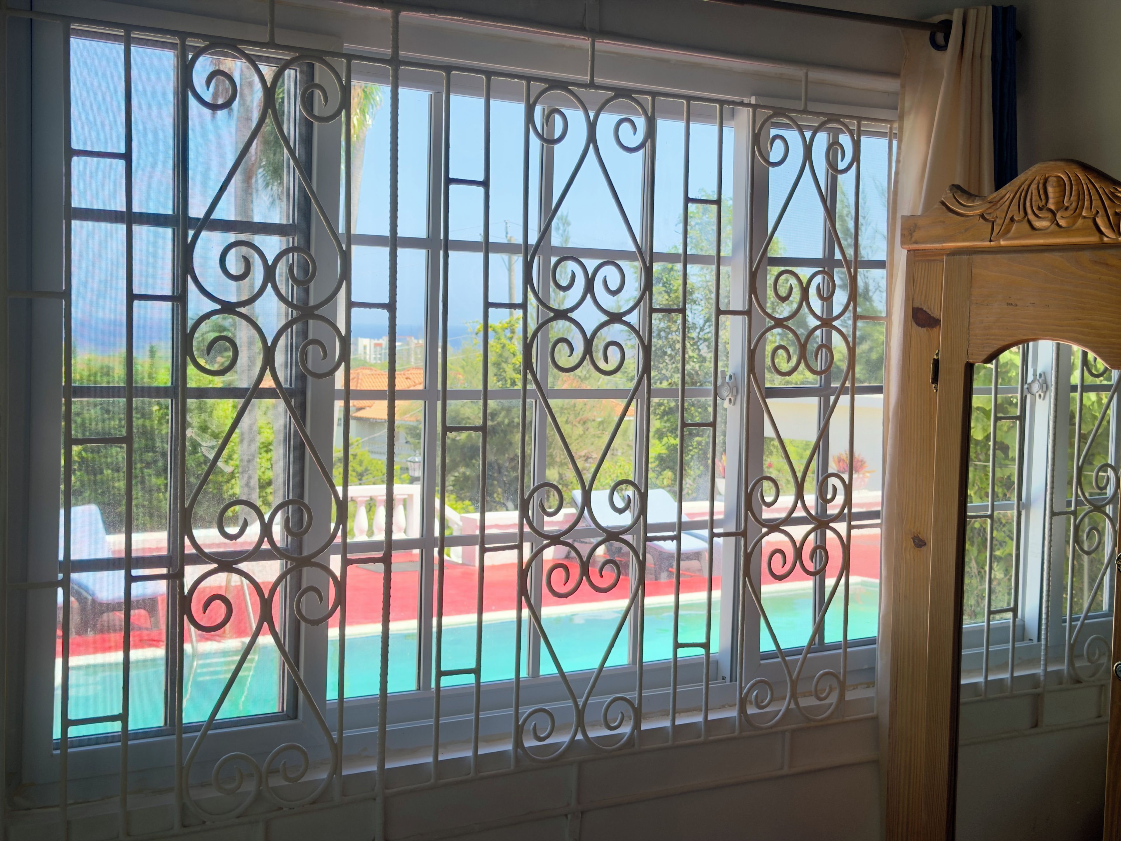 Janela com grades metálicas decorativas e vista para uma piscina.