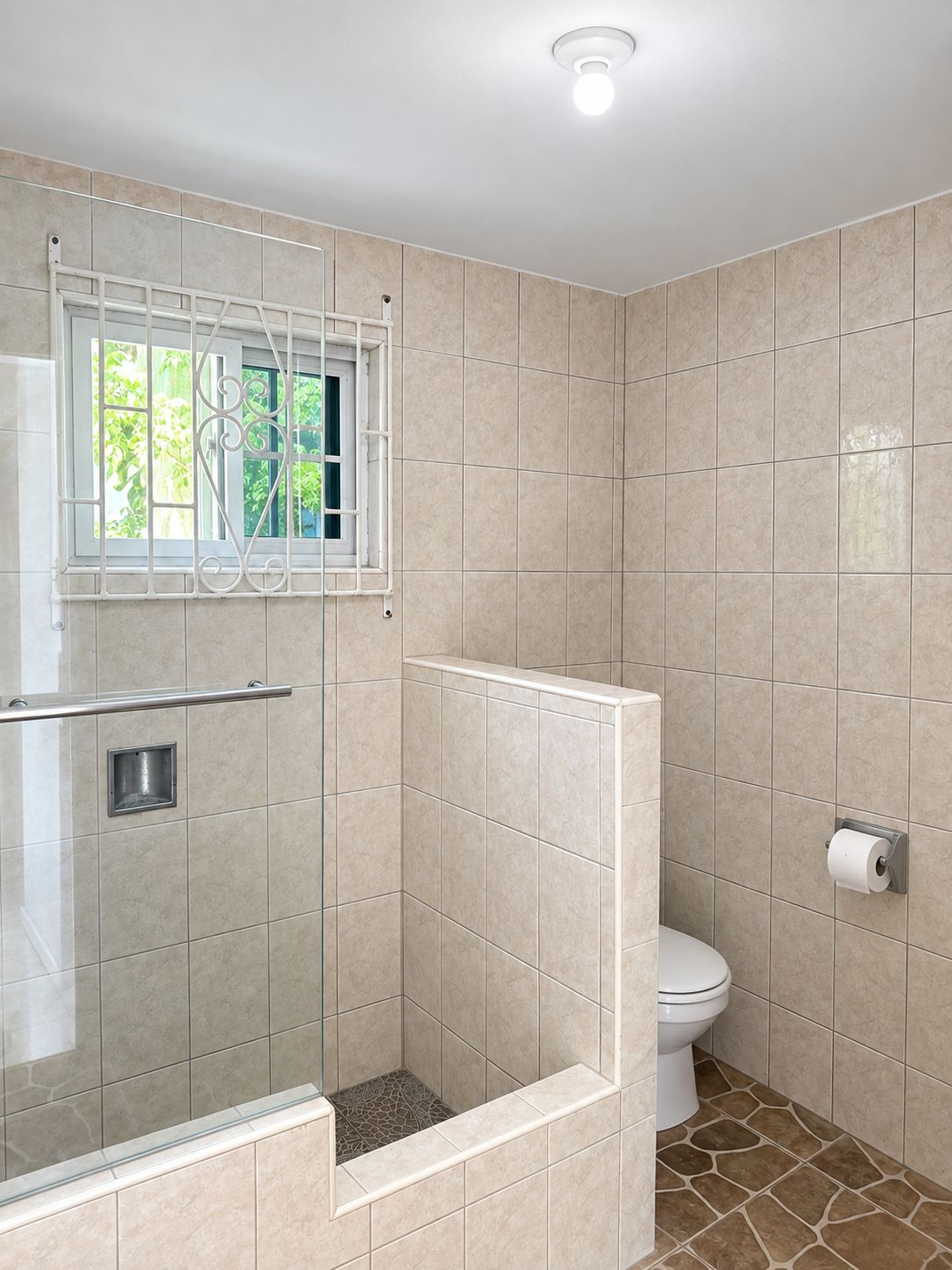 A bathroom with a shower, toilet, and a window with a metal railing.