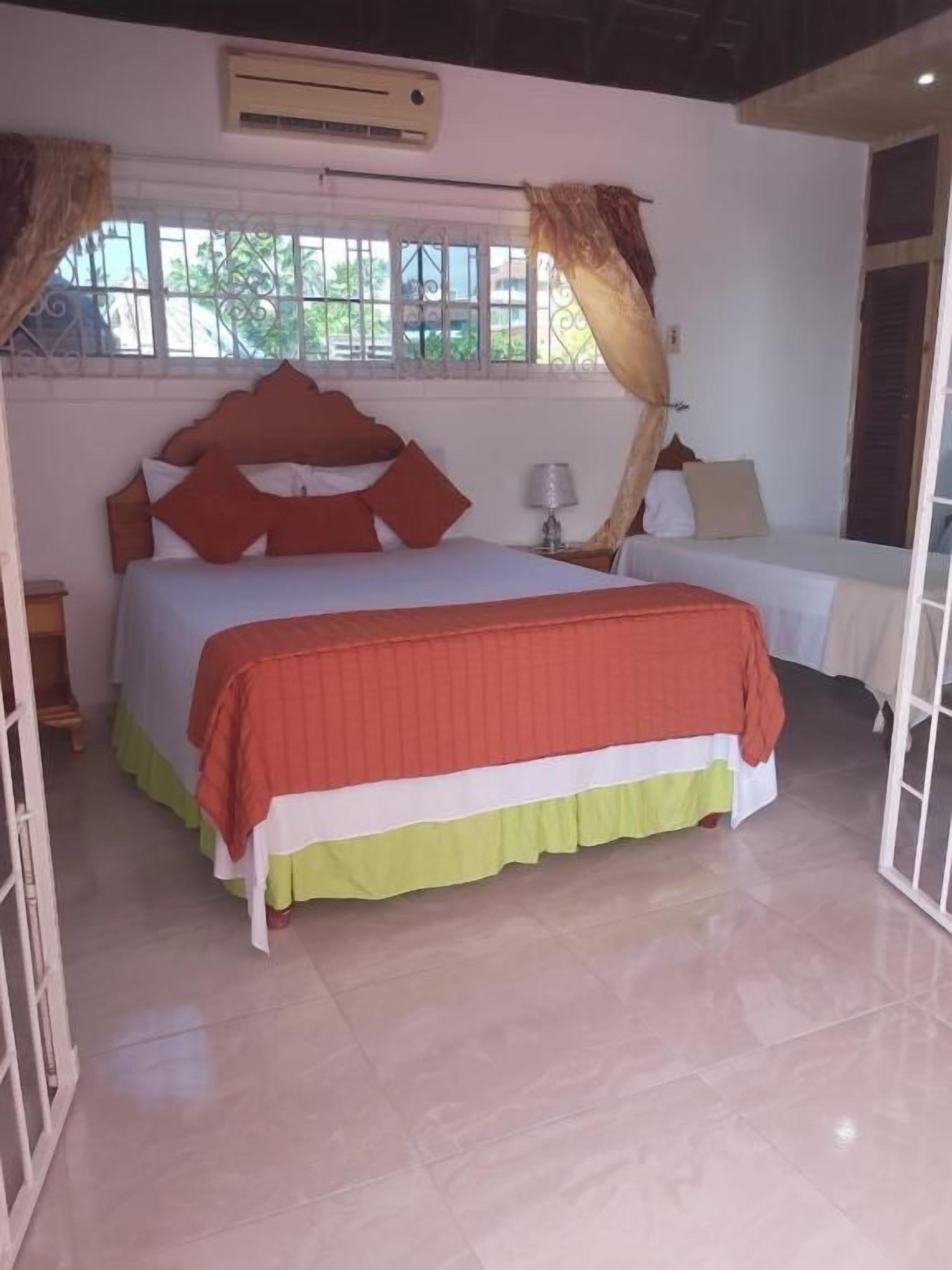 Un dormitorio con cama, cortinas, una ventana y una mesita de noche.