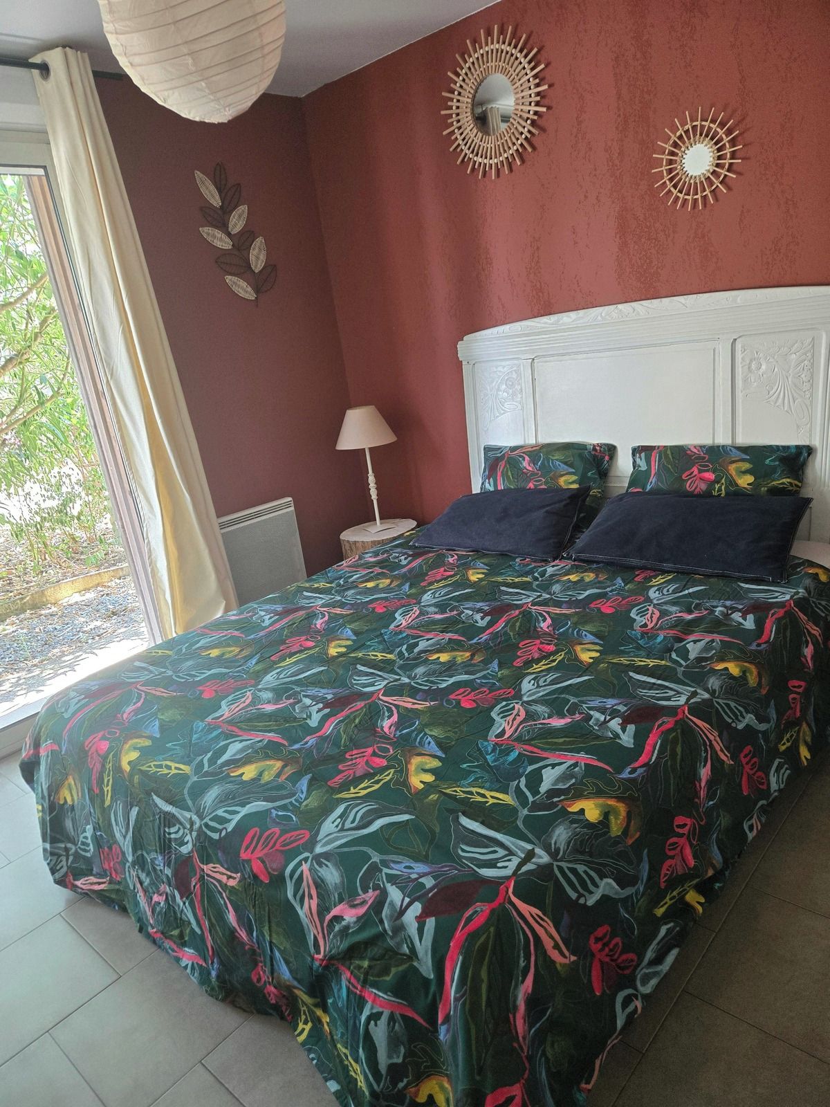 Une chambre à coucher avec un lit, une table de chevet, une lampe et une fenêtre avec des rideaux.