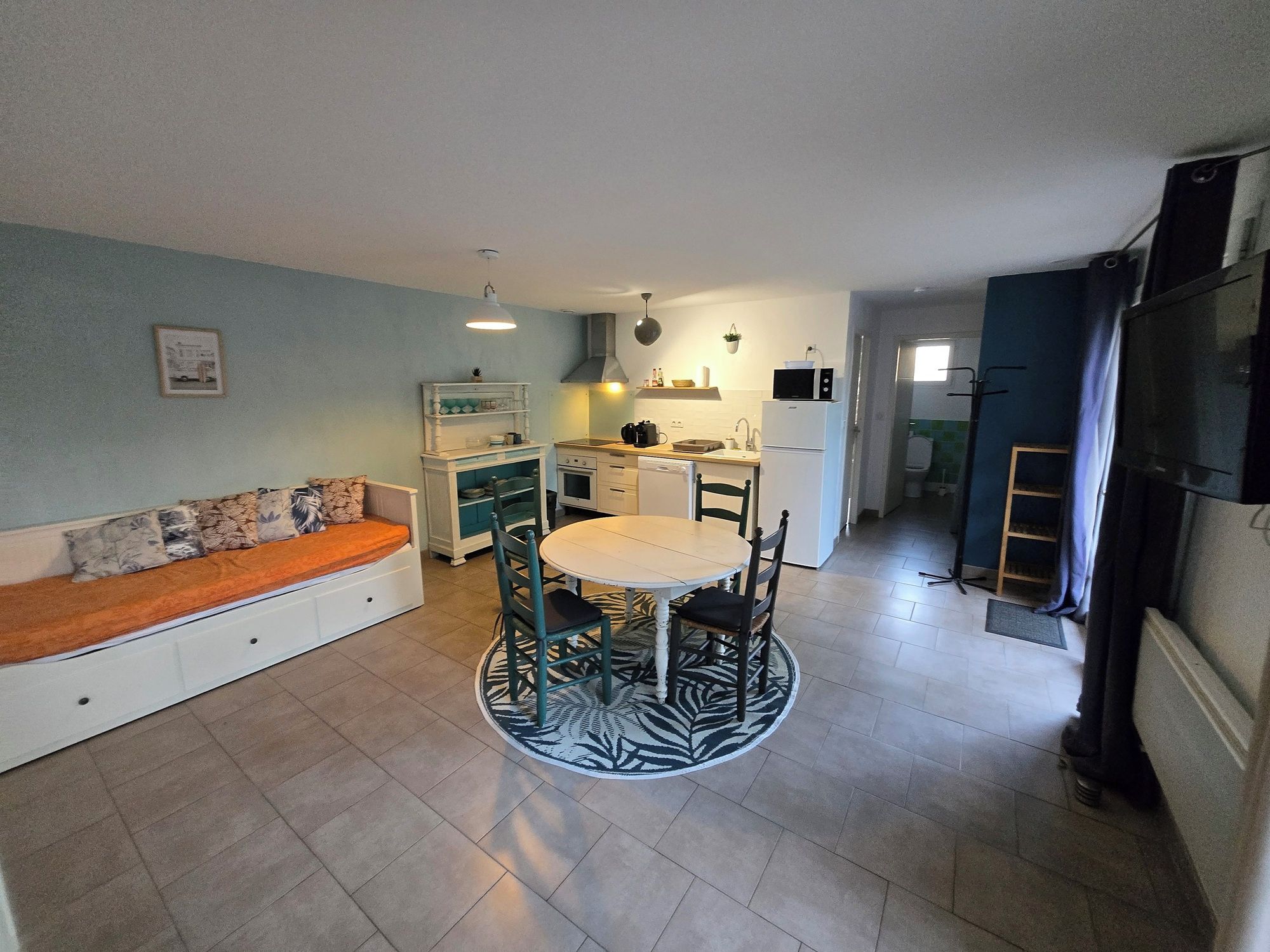 A compact kitchen with a dining area, a sofa, and a television.