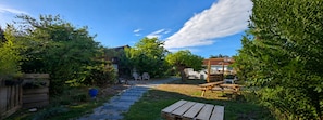 Un jardin avec un banc en bois, une table de pique-nique et un sentier menant à une maison.