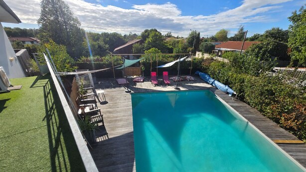 Una piscina con cubierta de madera, rodeada de vegetación y un cielo despejado.