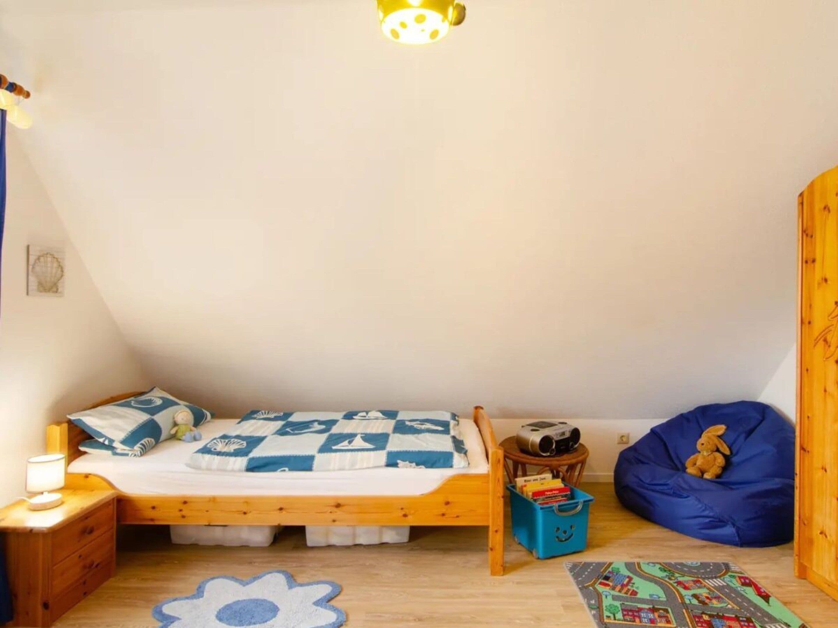 A child's bedroom with a single bed, a small side table, a bean bag, a bookshelf, and a wooden wardrobe.