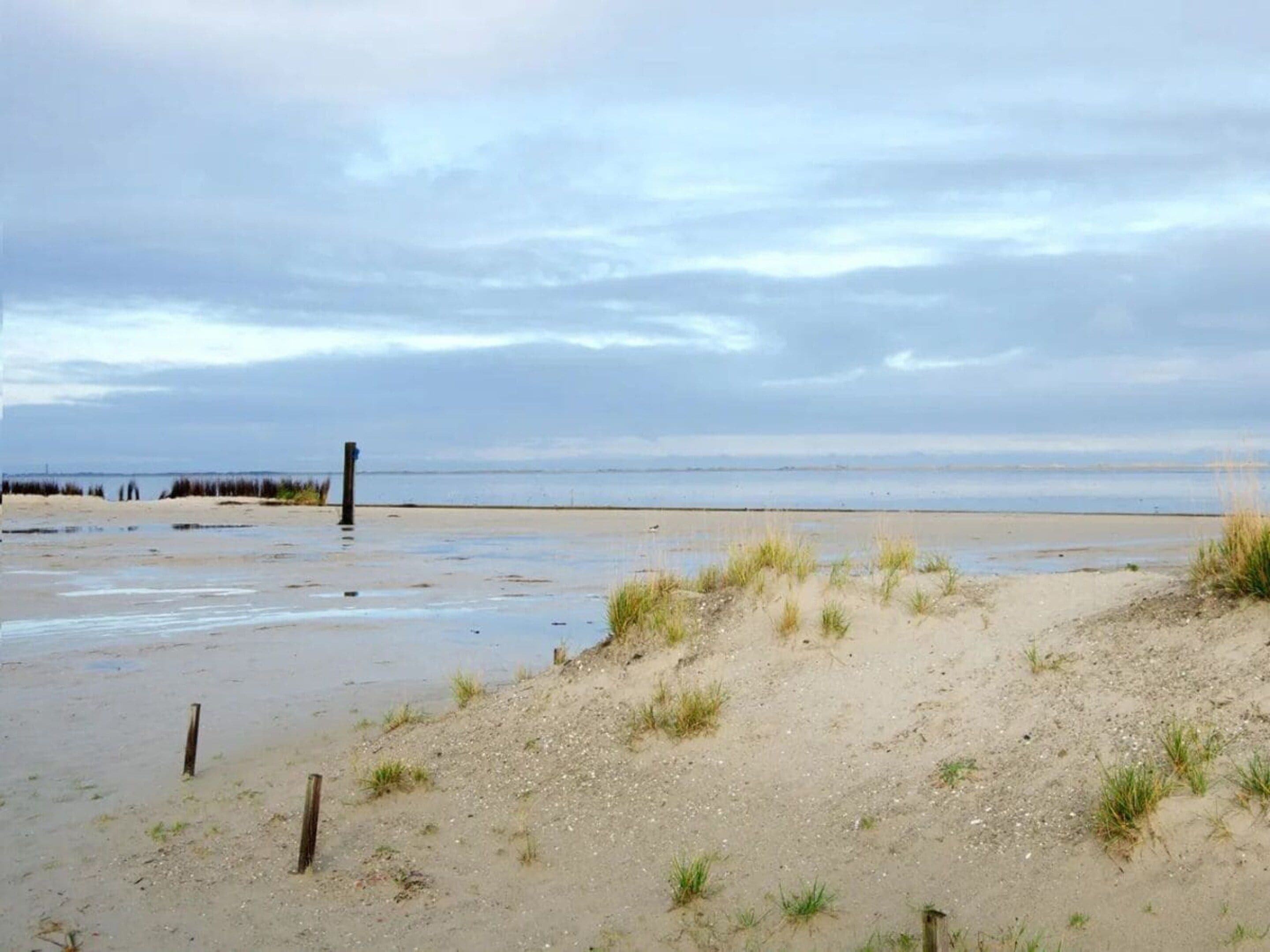 Una playa con dunas de arena y un poste de madera.