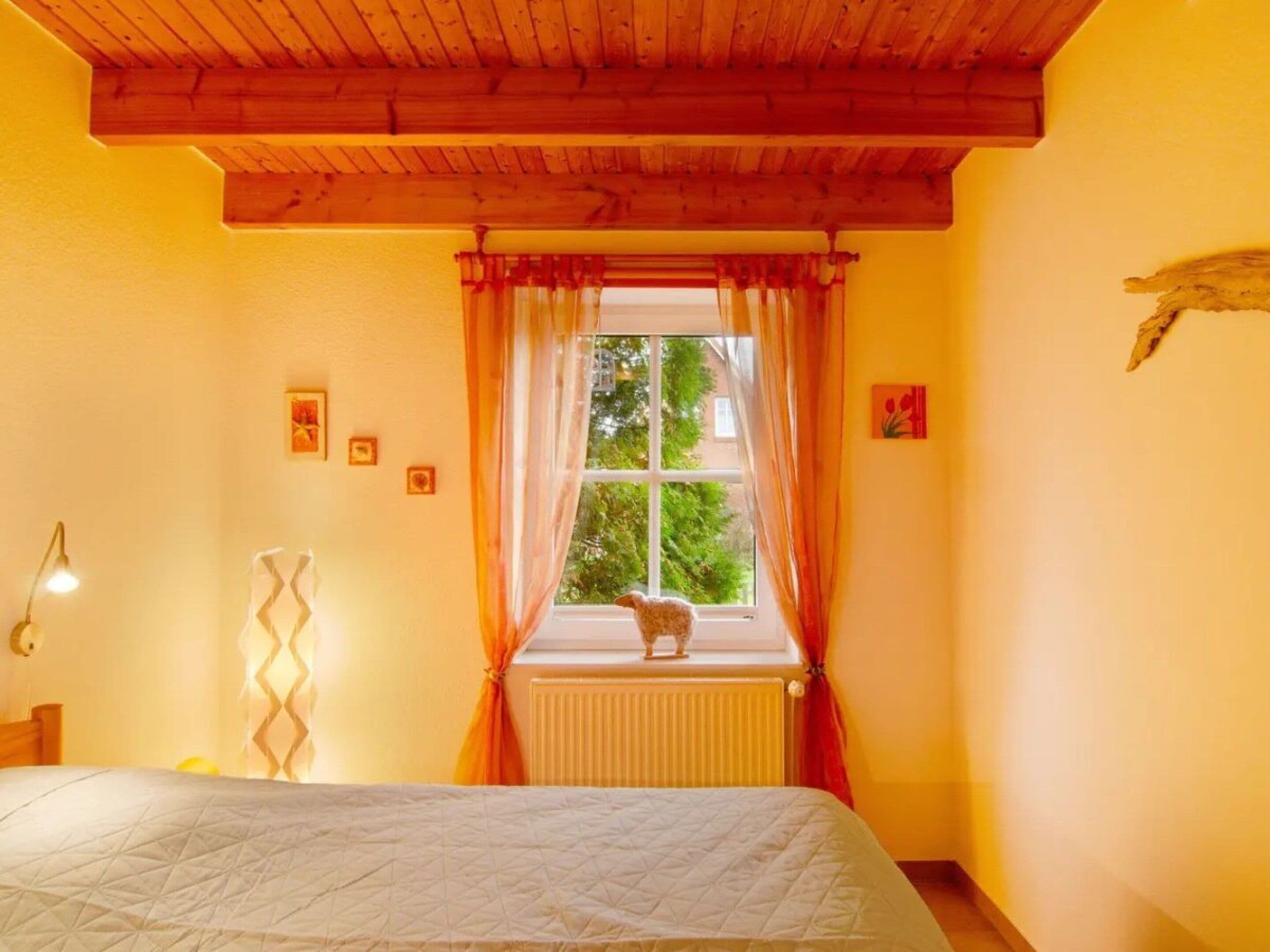 Un dormitorio con cama, ventana con cortinas, radiador y lámpara fijada a la pared.