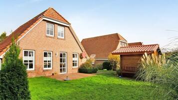 A two-story brick house with a sloped roof, a well-maintained lawn, and a small garden area.